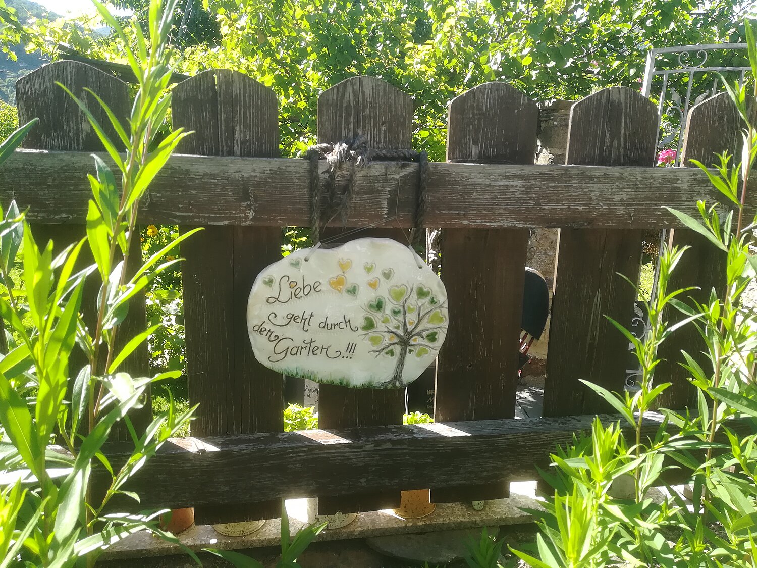 Keramikschild mit der Aufschrift "Liebe geht durch den Garten!" an einem Holzzaun.